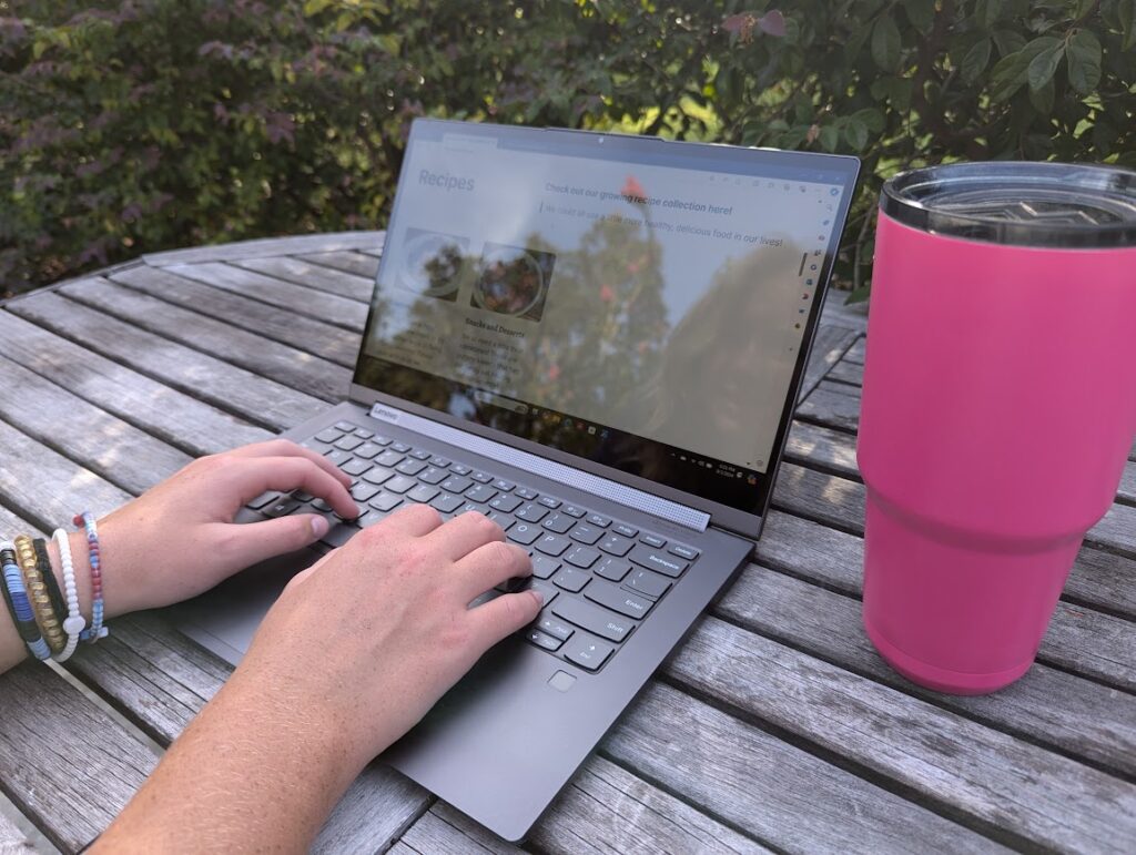 Laptop opened up with hands typing and cup of coffee to the side