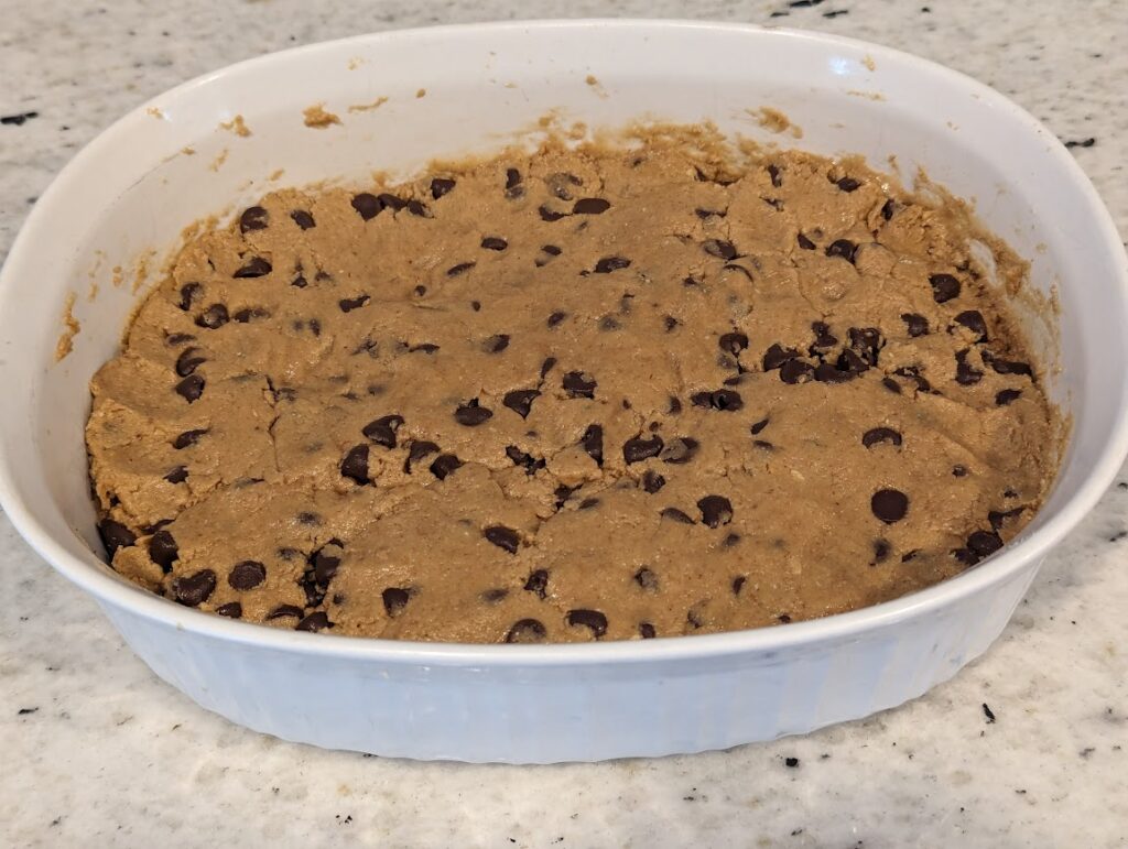 White baking dish with chocolate chip homemade perfect bars spread out and pressed down into the dish