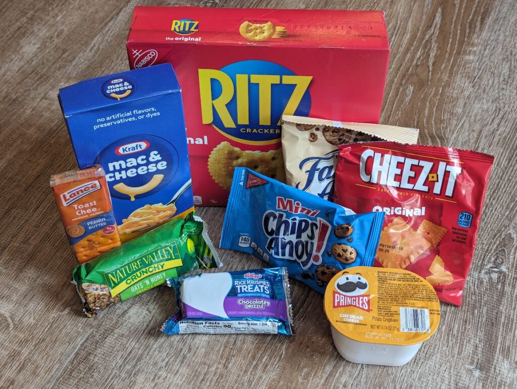 Boxed processed foods, including ritz crackers, mac & cheese, cheese sandwich crackers, nature valley crunchy bar, rice krispy treat, chips ahoy cookies, famous amos cookies, cheez-its, and pringles