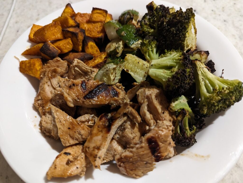 A perfect plate of food with half a plate of roasted broccoli and zucchini, one-fourth grilled chicken, and one-fourth roasted sweet potato