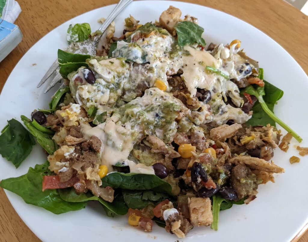 A chicken burrito bowl perfect plate with chicken, corn, beans, spinach, tomato, guacamole, rice, and sauce