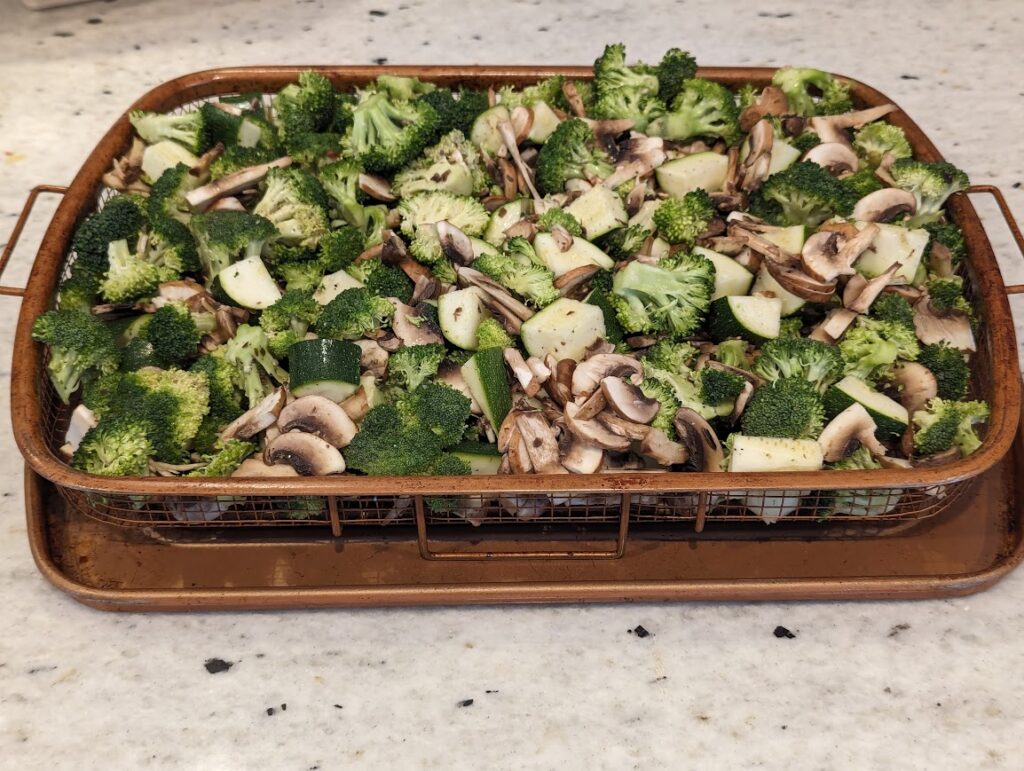 Sliced and seasoned broccoli, mushrooms, and zucchini on copper baking tray