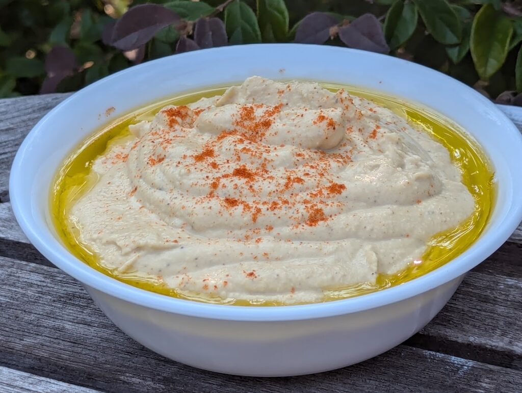 A bowl of hummus with olive oil around the edges and paprika sprinkled on top