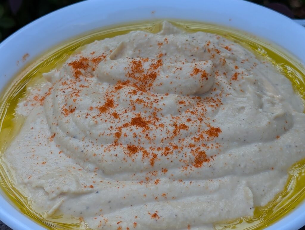 Up close view of a bowl of hummus with olive oil around the edge and paprika sprinkled on top